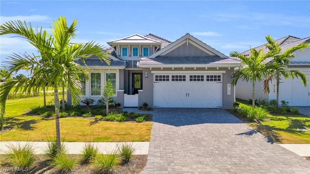 view of front facade with an attached garage, decorative driveway, a front yard, board and batten siding, and stucco siding