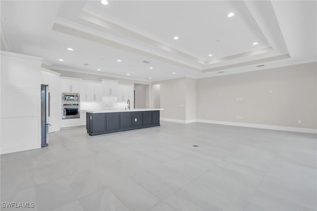 kitchen with appliances with stainless steel finishes, a tray ceiling, light countertops, white cabinetry, and a sink