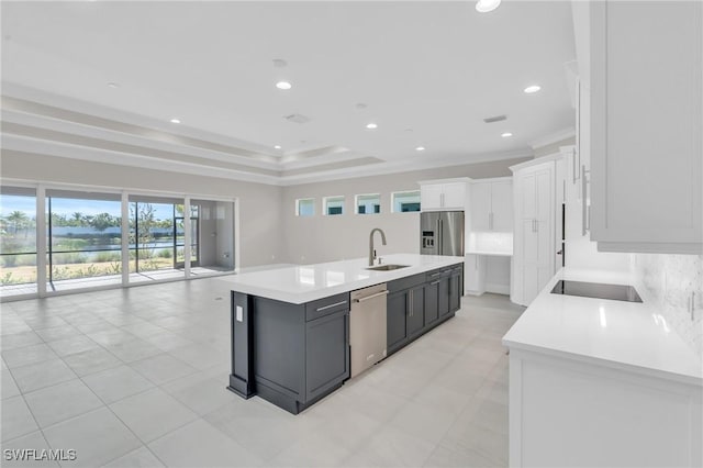 kitchen featuring a kitchen island with sink, stainless steel appliances, a sink, light countertops, and backsplash