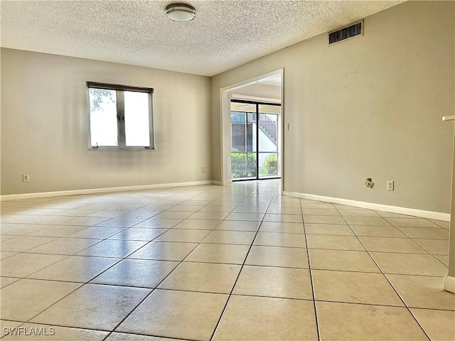 empty room featuring light tile patterned floors, a textured ceiling, and a healthy amount of sunlight