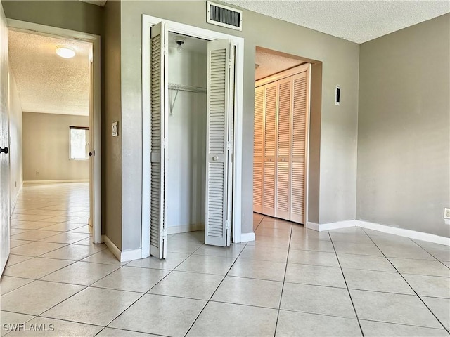 unfurnished bedroom with two closets, light tile patterned floors, and a textured ceiling