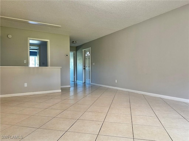 spare room with light tile patterned flooring, baseboards, and a textured ceiling