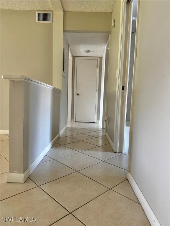 corridor featuring light tile patterned flooring, visible vents, a textured ceiling, and baseboards