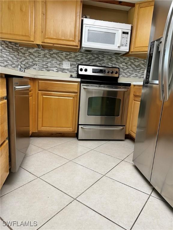 kitchen featuring light countertops, light tile patterned floors, decorative backsplash, appliances with stainless steel finishes, and brown cabinetry