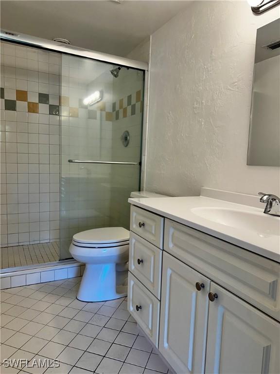 full bathroom with toilet, a stall shower, a textured wall, tile patterned floors, and vanity