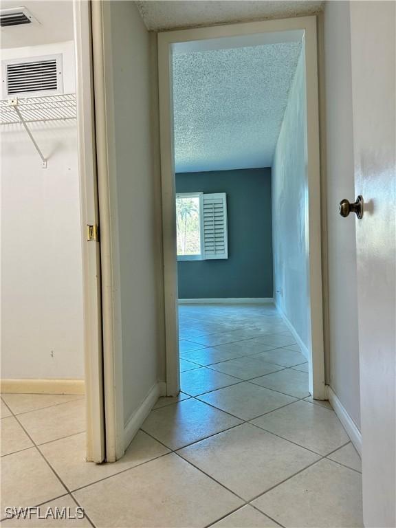 hallway with light tile patterned flooring, visible vents, a textured ceiling, and baseboards