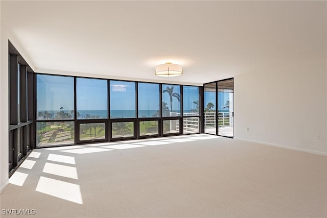 carpeted empty room featuring a wall of windows, a water view, and baseboards