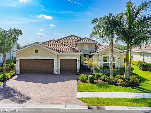 mediterranean / spanish-style home featuring a garage, a tile roof, stone siding, decorative driveway, and a front yard