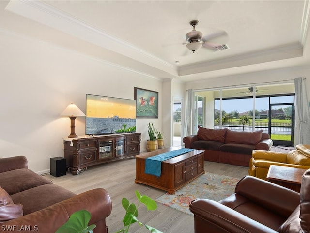 living room with a raised ceiling, ornamental molding, ceiling fan, and light hardwood / wood-style flooring