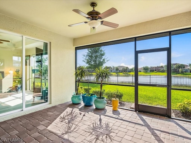 unfurnished sunroom with a ceiling fan and a water view