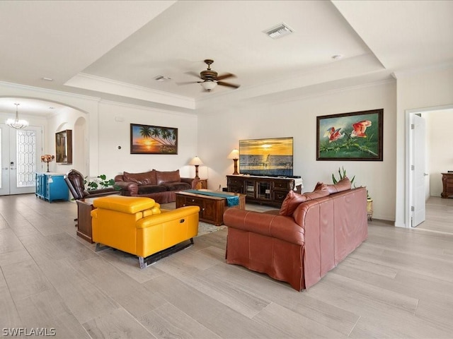 living room with visible vents, a tray ceiling, arched walkways, and ceiling fan with notable chandelier