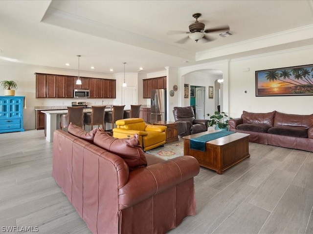 living area with arched walkways, visible vents, a ceiling fan, ornamental molding, and a raised ceiling