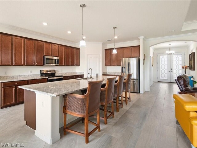 kitchen featuring pendant lighting, sink, a center island with sink, appliances with stainless steel finishes, and light stone countertops