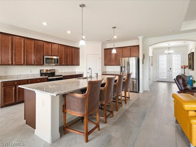 kitchen featuring arched walkways, appliances with stainless steel finishes, a kitchen breakfast bar, french doors, and a sink