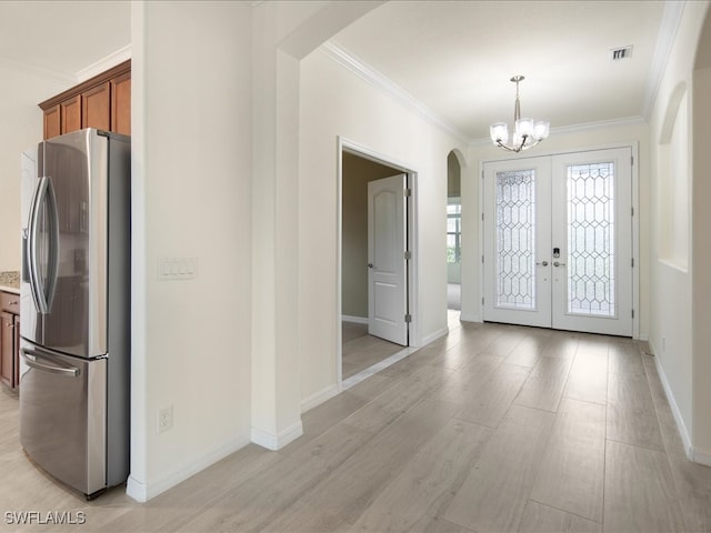 entrance foyer with light hardwood / wood-style floors, ornamental molding, an inviting chandelier, and french doors