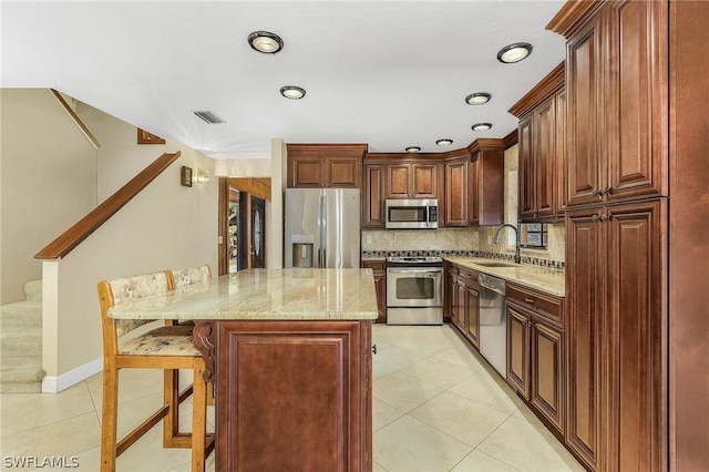 kitchen featuring light tile floors, tasteful backsplash, a breakfast bar area, appliances with stainless steel finishes, and light stone counters