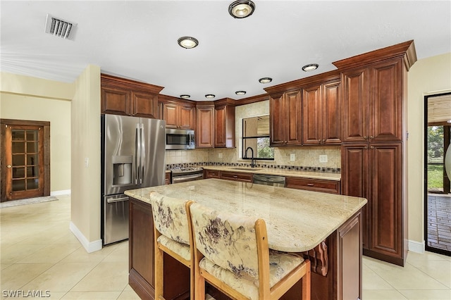 kitchen with backsplash, a kitchen breakfast bar, sink, stainless steel appliances, and a kitchen island