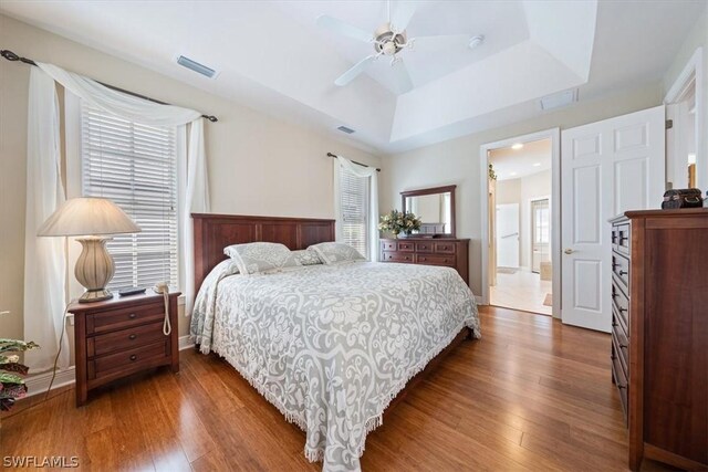 bedroom with a raised ceiling, connected bathroom, ceiling fan, and dark hardwood / wood-style flooring