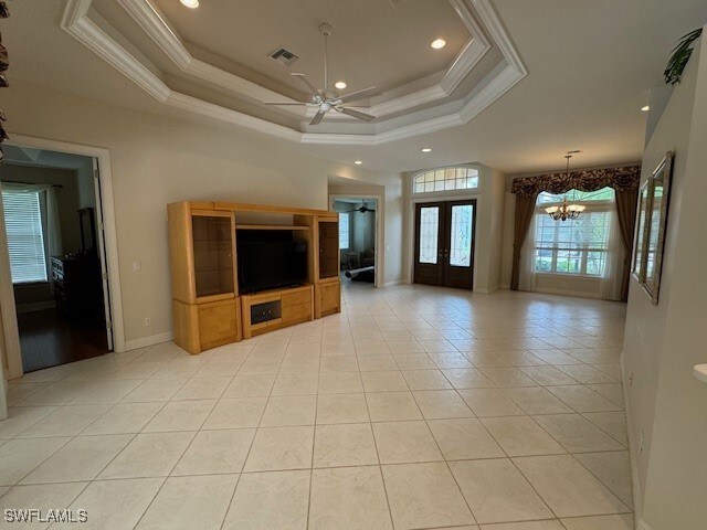 unfurnished living room featuring a tray ceiling, french doors, ceiling fan with notable chandelier, and light tile patterned floors