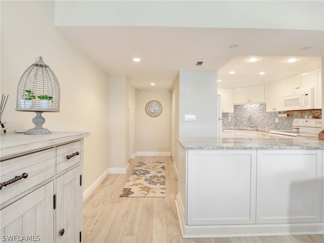 kitchen with white appliances, light stone counters, backsplash, light hardwood / wood-style floors, and white cabinetry