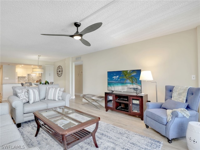 living room with a textured ceiling, ceiling fan, and light wood-type flooring