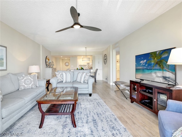 living room with ceiling fan, light wood-type flooring, and a textured ceiling