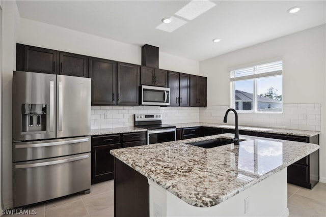 kitchen featuring light stone countertops, appliances with stainless steel finishes, decorative backsplash, sink, and a center island with sink