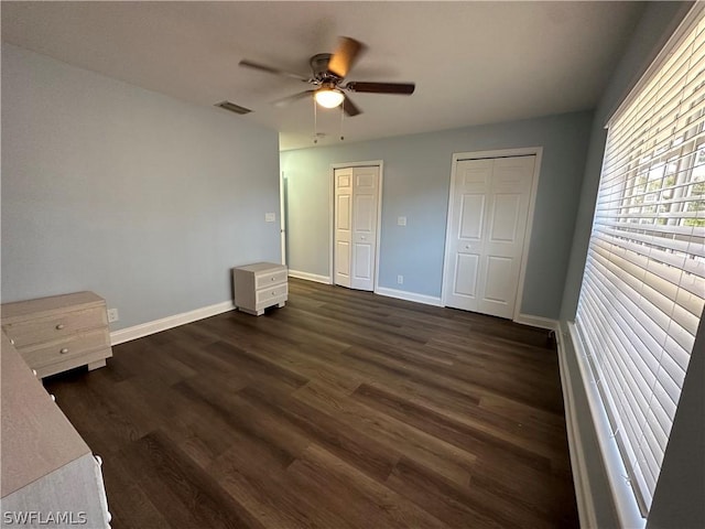 unfurnished bedroom featuring baseboards, visible vents, dark wood-style floors, ceiling fan, and two closets