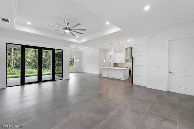 unfurnished living room with a raised ceiling, ornamental molding, ceiling fan, and tile flooring