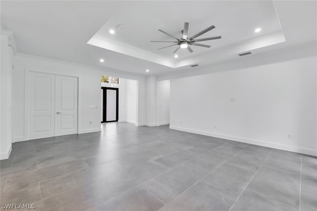 tiled empty room with ceiling fan, a raised ceiling, and ornamental molding