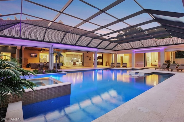 pool at dusk with glass enclosure, a patio area, and an in ground hot tub