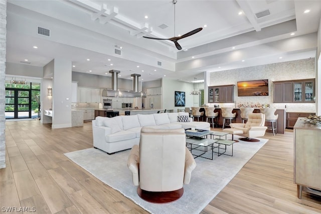 living room featuring light hardwood / wood-style flooring, coffered ceiling, a high ceiling, beam ceiling, and ceiling fan with notable chandelier