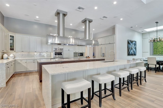 kitchen featuring light stone counters, a breakfast bar, white cabinetry, a chandelier, and a kitchen island with sink