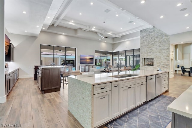 kitchen with an island with sink, light hardwood / wood-style floors, beam ceiling, light stone countertops, and sink