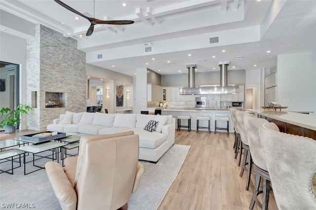 living room featuring coffered ceiling, beam ceiling, a fireplace, ceiling fan, and light wood-type flooring