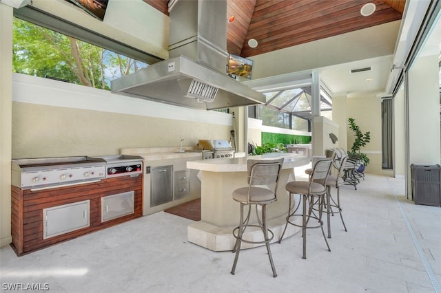 kitchen with island range hood, light tile floors, wood ceiling, a breakfast bar, and a high ceiling