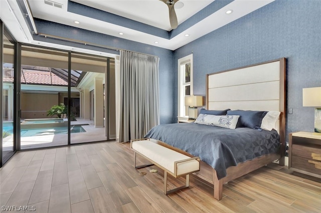 bedroom with a raised ceiling, light hardwood / wood-style floors, and access to exterior