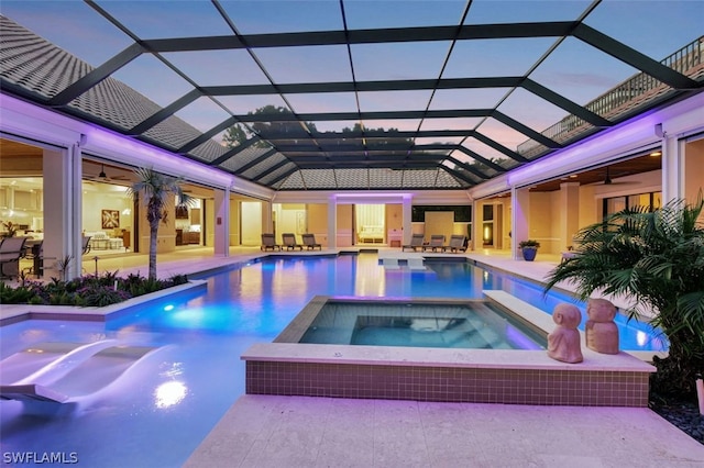 pool at dusk with a patio area, an in ground hot tub, ceiling fan, and glass enclosure