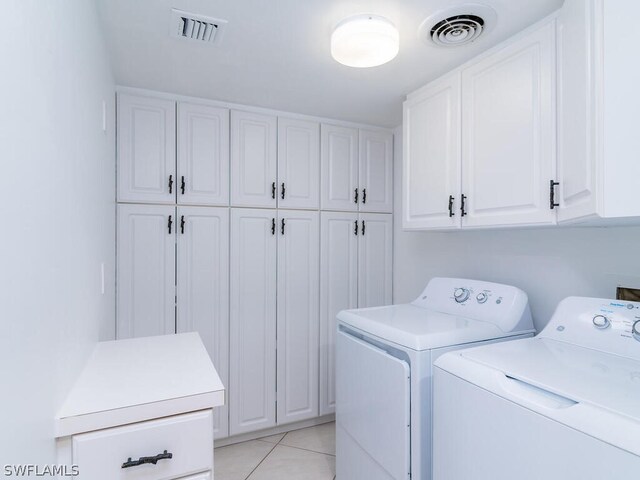 clothes washing area featuring washer and clothes dryer, cabinets, and light tile patterned floors