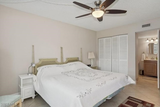 bedroom featuring ceiling fan, light tile patterned floors, a textured ceiling, a closet, and ensuite bathroom