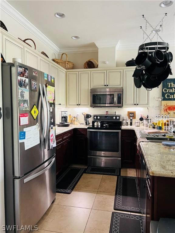 kitchen with light stone counters, crown molding, stainless steel appliances, cream cabinets, and light tile patterned flooring