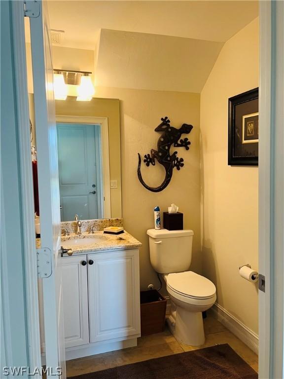 half bathroom featuring vaulted ceiling, vanity, toilet, and baseboards