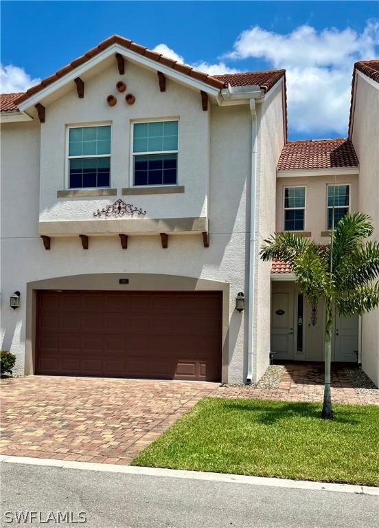 mediterranean / spanish-style home with decorative driveway, a tile roof, an attached garage, and stucco siding