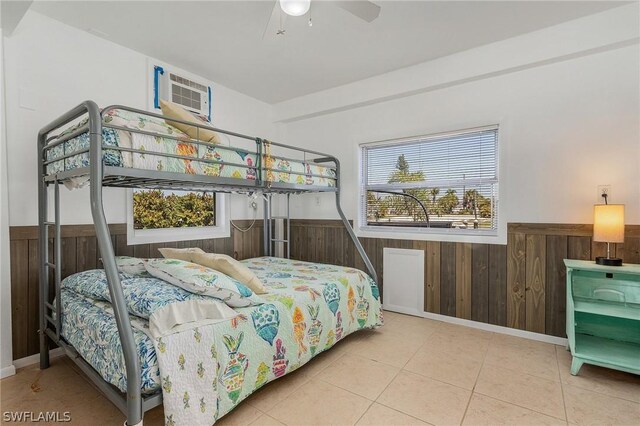 bedroom featuring a wall mounted AC, ceiling fan, light tile patterned floors, and wooden walls