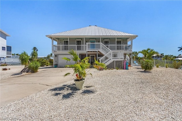 beach home with stairway, concrete driveway, covered porch, metal roof, and a garage