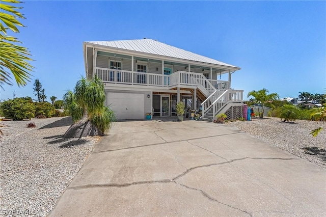 coastal home featuring covered porch, stairs, concrete driveway, a garage, and metal roof