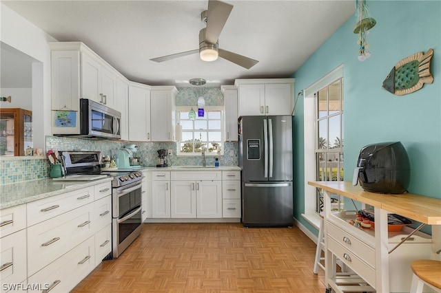 kitchen featuring light parquet floors, appliances with stainless steel finishes, sink, ceiling fan, and white cabinets