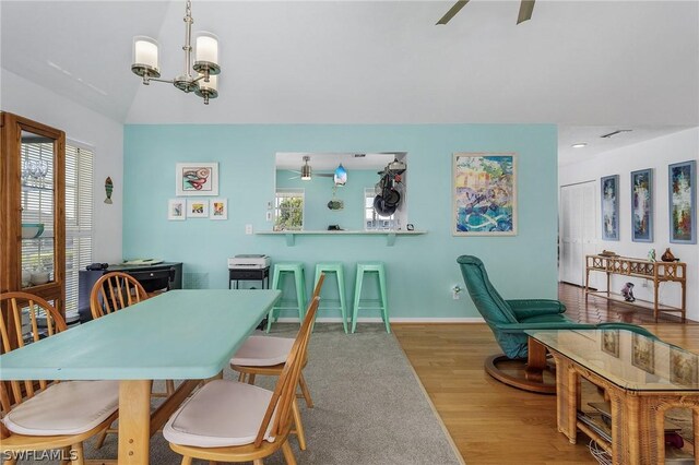 dining space with ceiling fan with notable chandelier, wood-type flooring, and vaulted ceiling