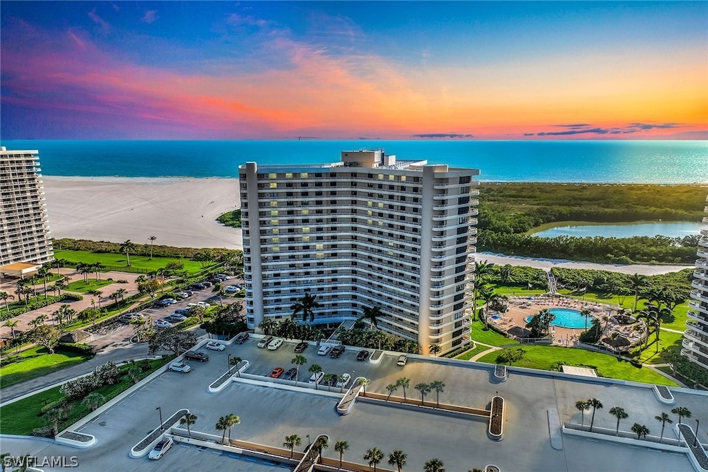 aerial view at dusk with a water view and a view of the beach