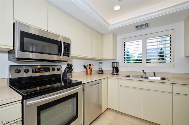 kitchen with sink, cream cabinetry, a tray ceiling, light tile patterned floors, and appliances with stainless steel finishes